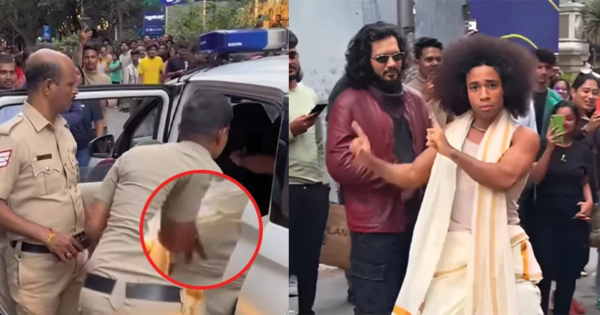 A police officer places a man in a patrol car, while on the right, a man in traditional attire energetically performs on a street, attracting a crowd. নোয়েল রবিনসন.