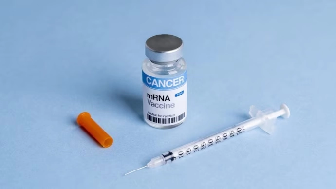 A vial labeled "Cancer mRNA Vaccine" and a syringe with an orange cap lie on a light blue surface, symbolizing hope and scientific progress in cancer treatment.